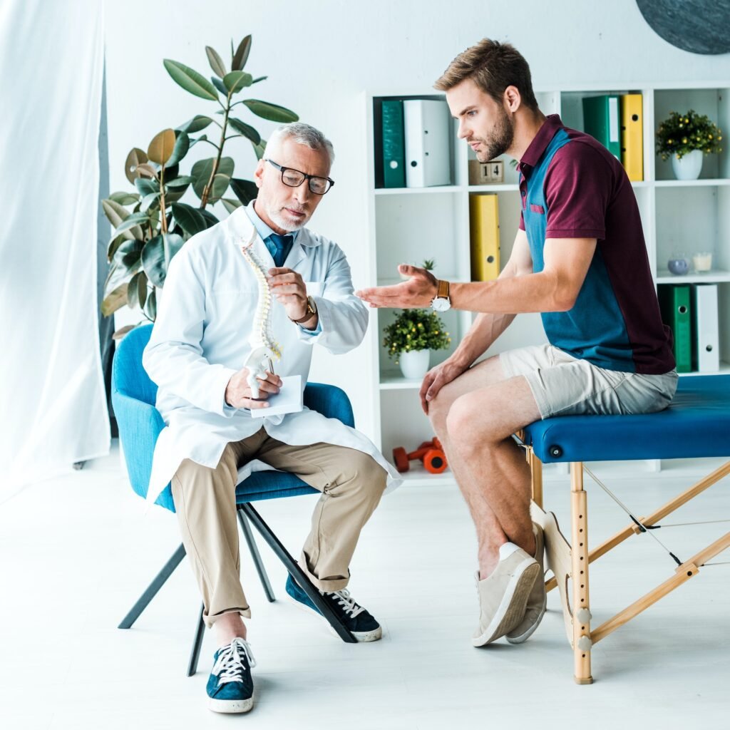 handsome bearded man gesturing while looking at spine model near doctor in glasses