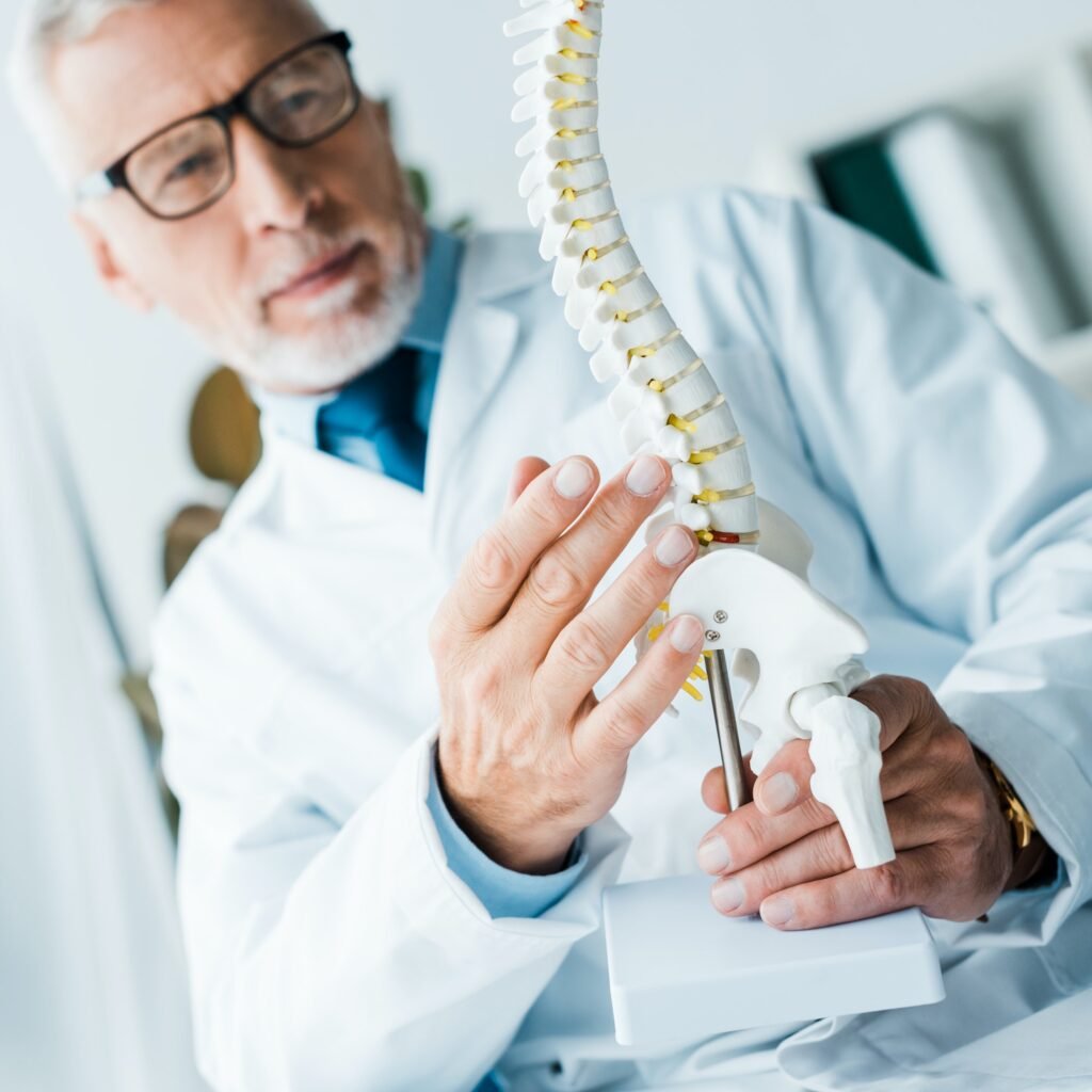 selective focus of bearded doctor in white coat holding spine model in clinic